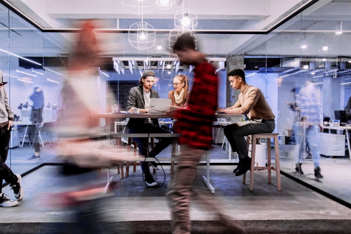 A time lapse of an open-office layout with employees walking in the foreground and others collaborating in the background