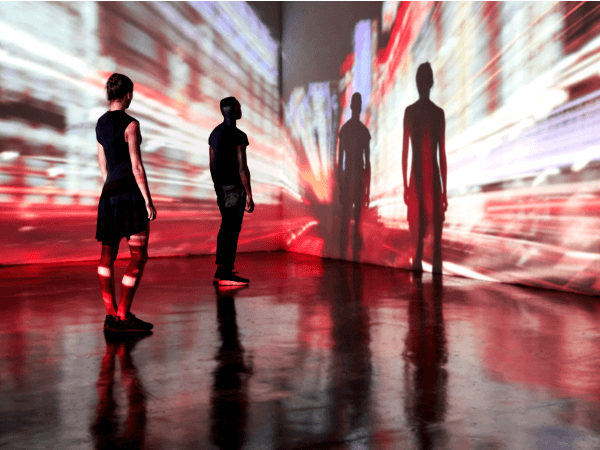 Dos personas proyectan sus sombras sobre un paisaje urbano proyectado en una pared.