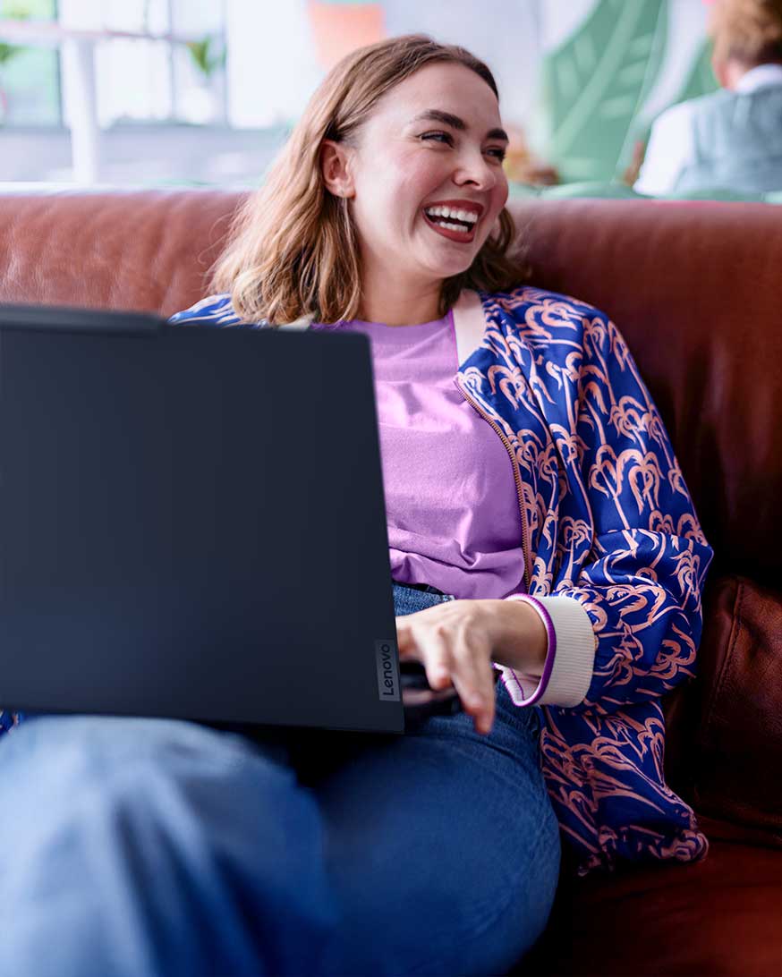 A woman sitting on a couch using her laptop and laughing. 