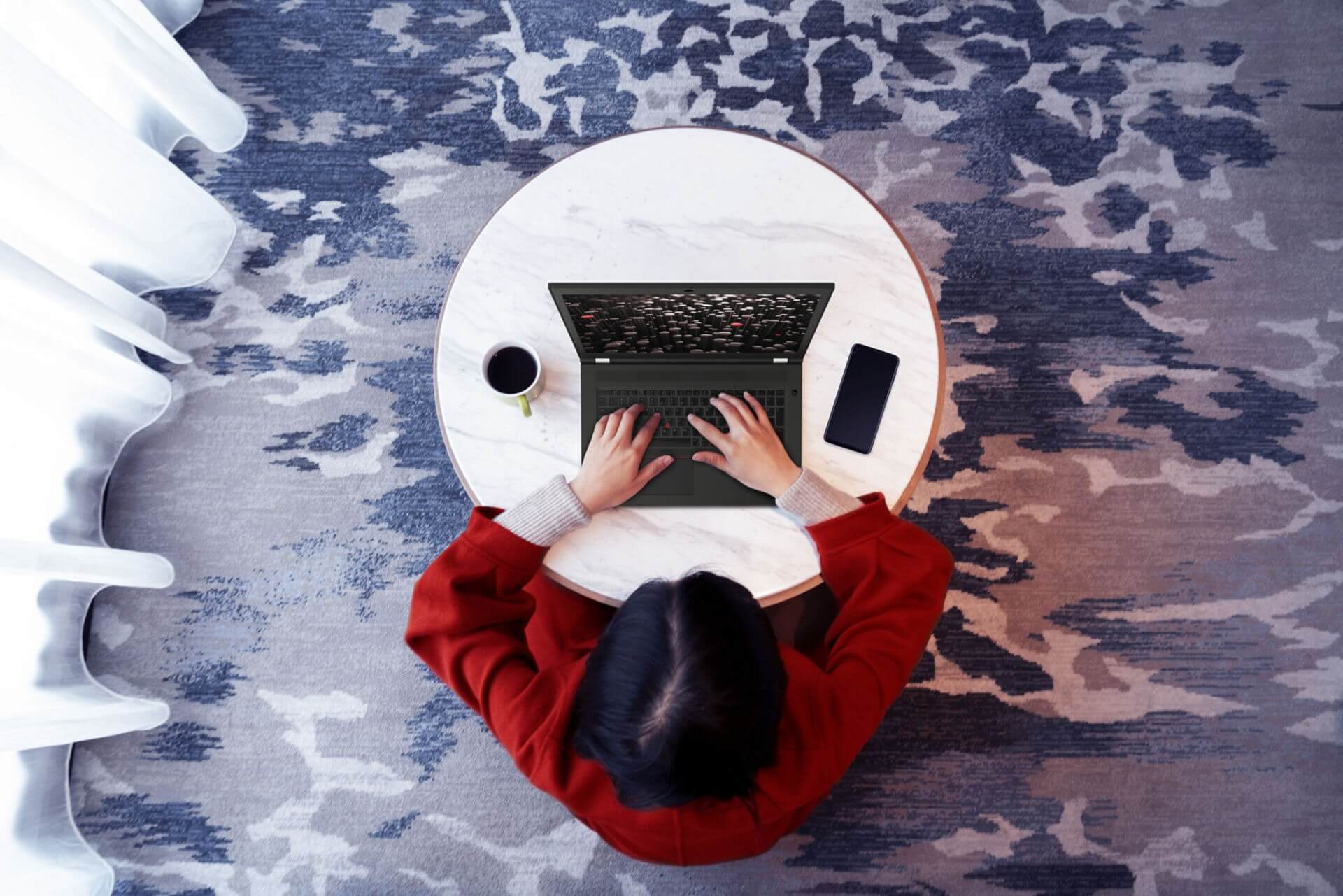 An overhead shot of a Lenovo employee using a laptop at a small round table. 