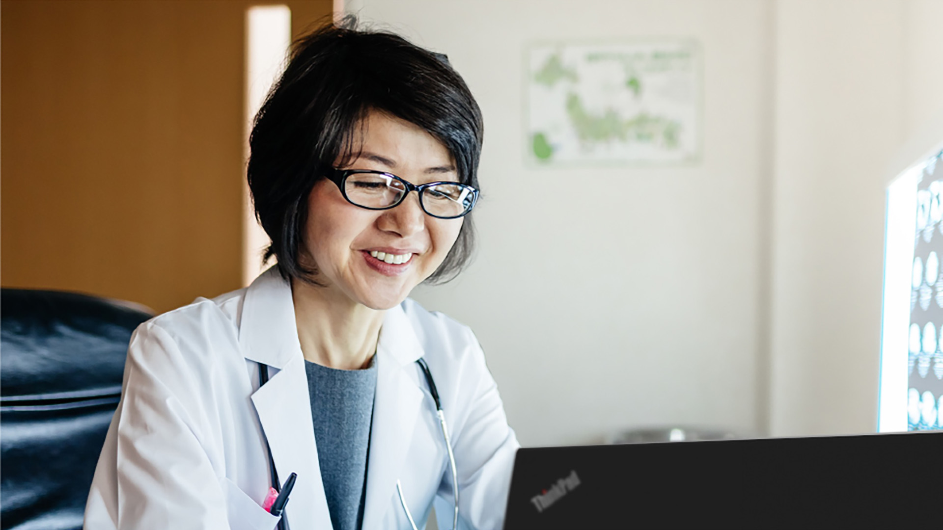 A doctor smiles while looking at her ThinkPad laptop