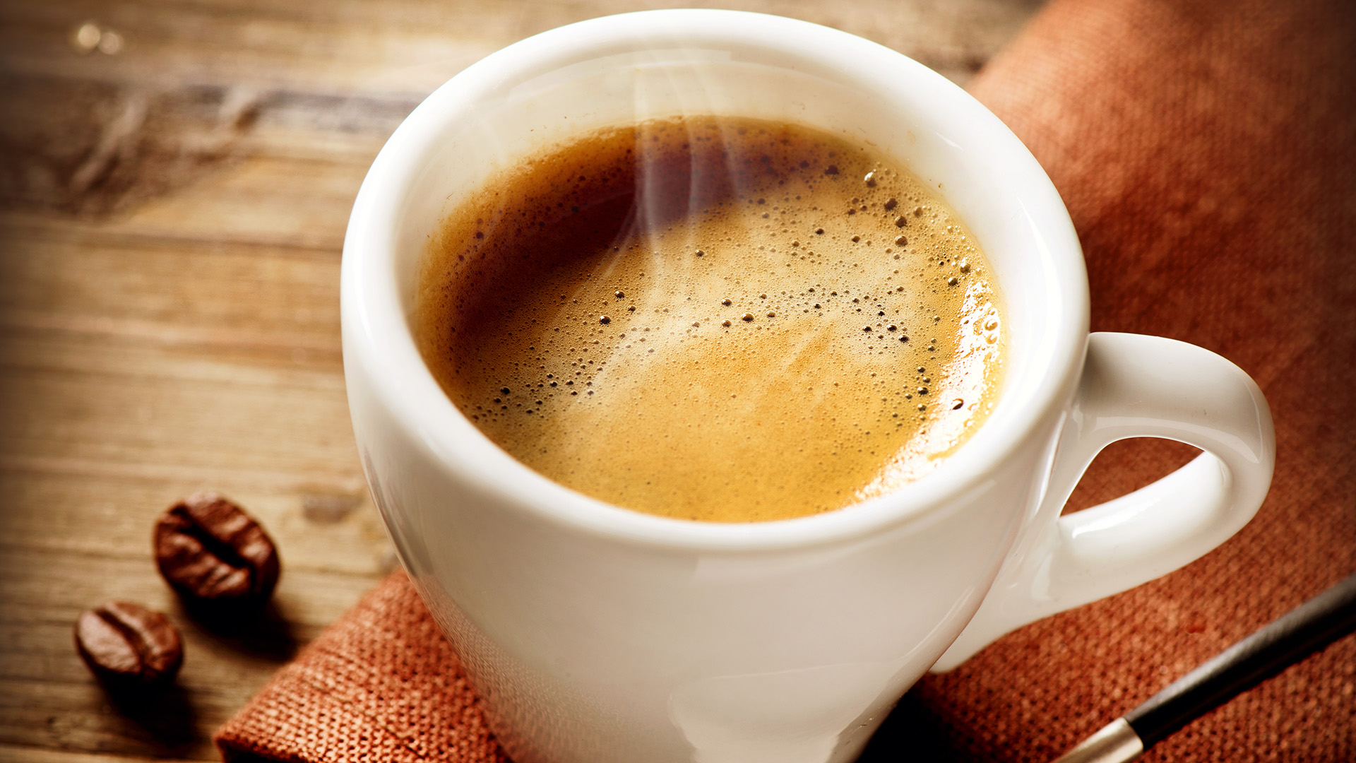 Une tasse de café chaud, une cuillère et des grains de café