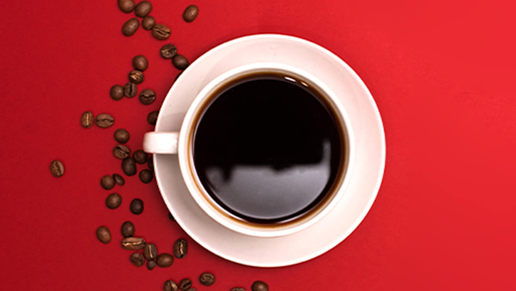 Vue aérienne du café dans une tasse blanche sur une soucoupe avec des grains de café dispersés autour