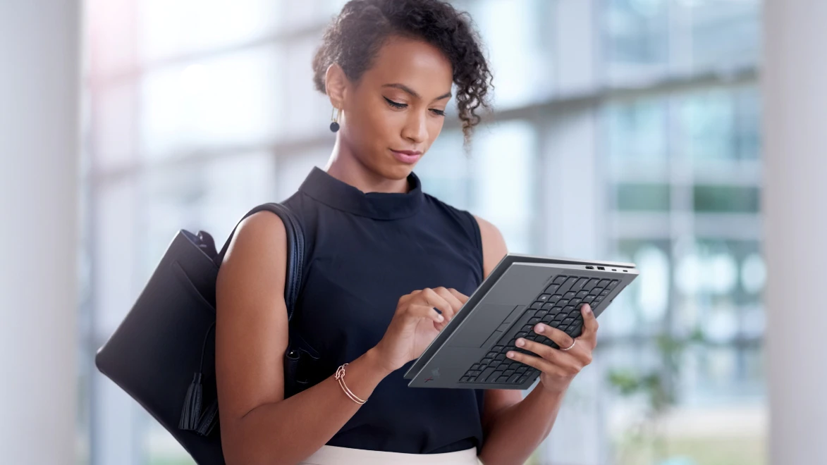 Business woman using Lenovo ThinkPad X1 Yoga Gen 7 in tablet mode, while standing near wall of glass.