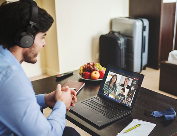 A man in a headset, facing right, talks with others shown on-screen on a ThinkPad X13 Gen 4 laptop