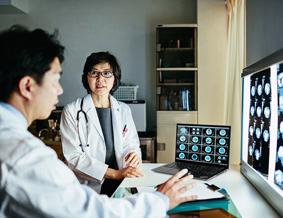 Two medical professionals discussing brain scans on transparencies in front of a lighted screen on a table, with a ThinkPad P14s Gen 4 (14