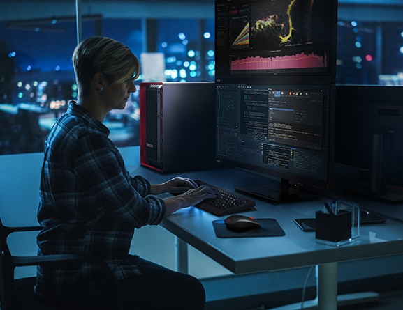 Software engineer working at night, looking at large monitor, using a laptop to code, with Lenovo ThinkStation PX workstation stood vertically on desk