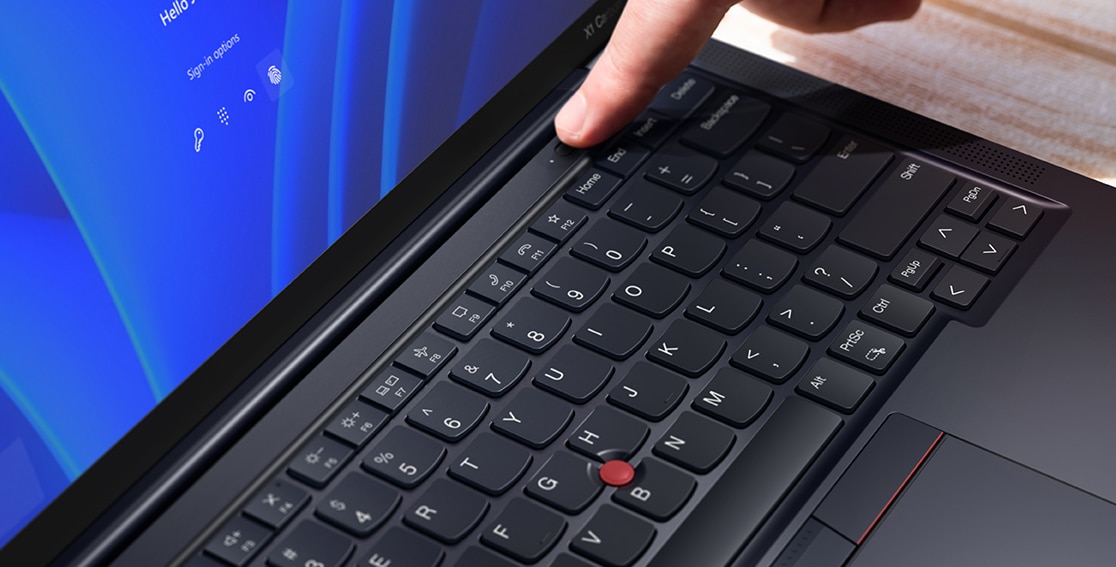 Detalj av ett finger som rör vid strömbrytaren med inbyggd fingeravtrycksläsare på den bärbara datorn Lenovo ThinkPad X1 Carbon Gen 11.