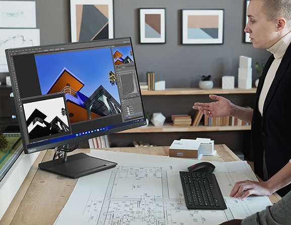 Architect in an office,  with drawings on desk next to mouse & keyboard, looking at designs on the screen of ThinkCentre Neo 30a  (27