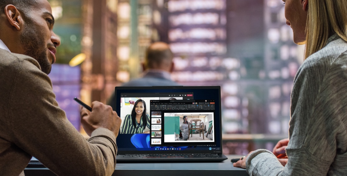Kaksi henkilöä pöydän ääressä ja heidän välissään Lenovo ThinkPad X1 Carbon Gen 11 -kannettava, näytöllä näkyvissä videoneuvottelu.
