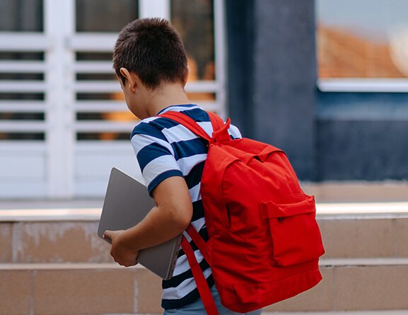 Elementary school student walking into a building while holding a Lenovo 100w Gen 4 (11” Intel) laptop