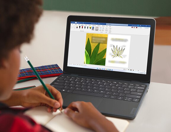 Elementary school student taking notes while looking at the display of a Lenovo 100w Gen 4 (11” Intel) laptop