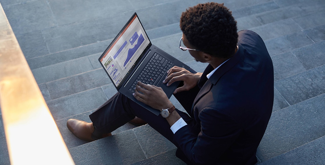 Young black man in a suit sitting on concrete steps with a Lenovo ThinkPad X1 Extreme Gen 4 laptop open on his lap.