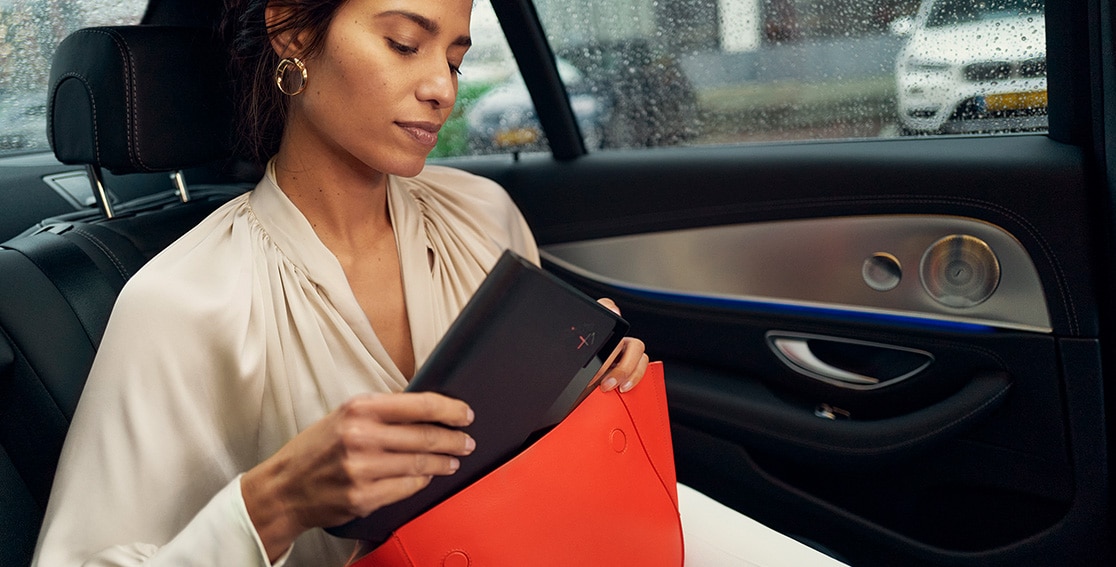 Woman sitting in a car pulling a folded Lenovo ThinkPad X1 Fold out of her red handbag