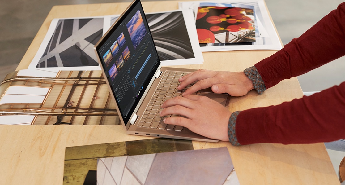 Someone working with a Yoga C740 in laptop mode, on a desk covered with design photographs