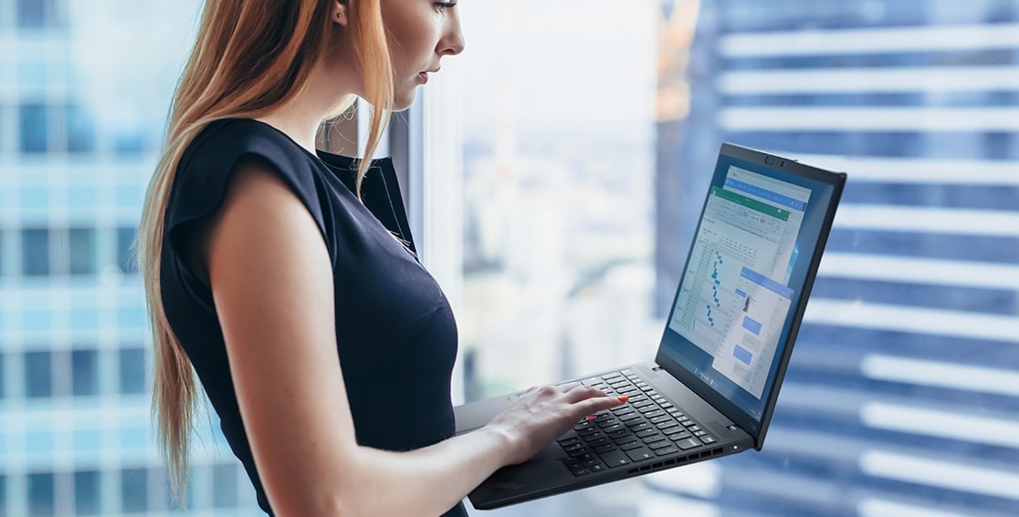 Mujer sosteniendo un Lenovo ThinkPad X1 Nano mientras escribe en el teclado, con varios gráficos en pantalla.
