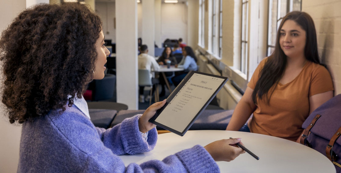 Deux personnes dans un café, l’une tenant une liseuse Lenovo Smart Paper E-Ink posée à plat et prenant des notes sur l’écran avec un Lenovo Smart Pen