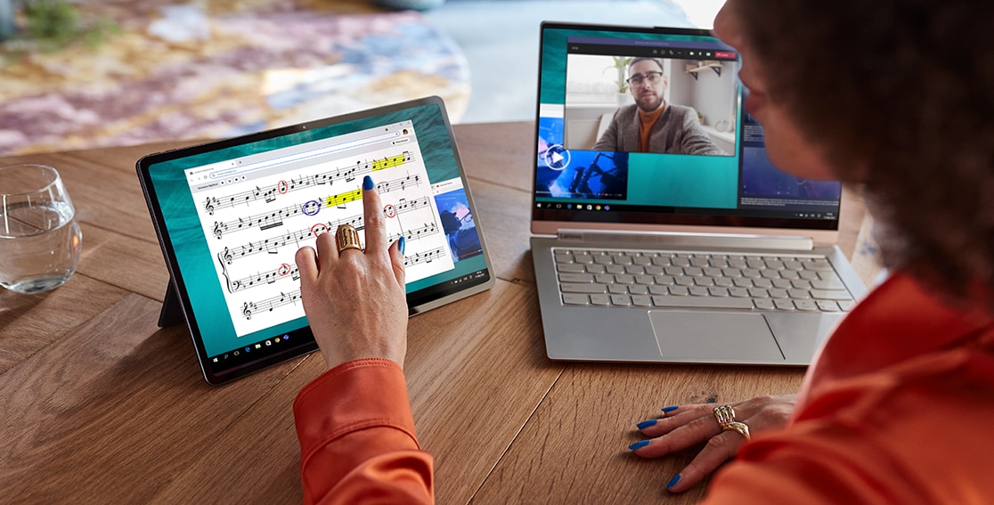 The Lenovo Tab P12 Pro rests on its stand at a 70-degree angle as a person uses it as a wireless second display for the open laptop sitting beside it.