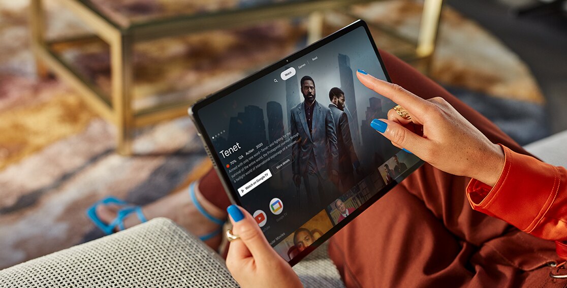 A person holds the Lenovo Tab P12 Pro before them, using a finger to control an on-screen movie app, with more app icons across the bottom of the screen.