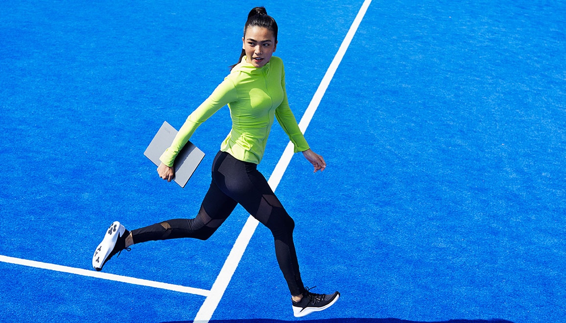 Woman running across tennis court holding Yoga S Series laptop.